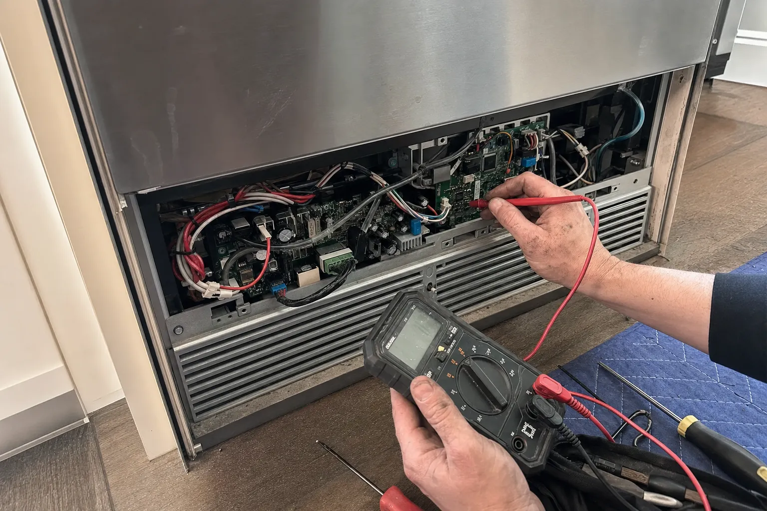 Multimeter probe on the control board bay behind an undercounter unit's lower grille